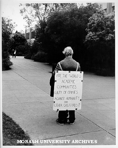 Sandwich board demonstrator, Open Day. 'Are the World's Academic Communities Guilty of Crimes Against Humanity and Other Creatures?'