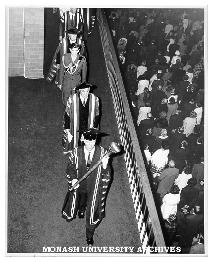 Academic procession leaving Robert Blackwood Hall after opening ceremony led by Comptroller Mr F. H. Johnson bearing Mace