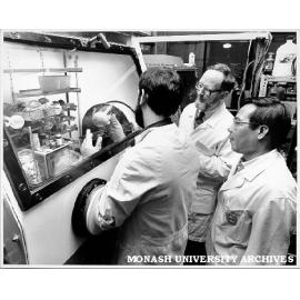 Student Dallas Wilkinson handling rare earth compound inside dry box, watched by Dr Glen Deacon (centre) and Dr Tran Tuong