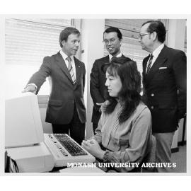 Visitor Miss Shigeko Nakamura using Epson QC 10 microcomputer with English and Japanese keyboard, watching from left: Mr Dan Price and Mr Shuzo Isoda from Epson Australia, and Professor Jiri Neustupny