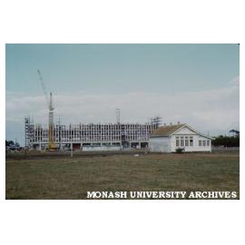 Humanities building, first stage under construction, old school house in foreground