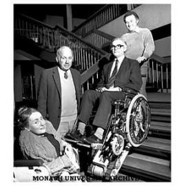 Stair-climbing wheelchair with designing engineer John Buckland (top), Safety Office Will Barker (in chair), Director of Health Services Dr John Green and Diploma of Education student Sue Shaw